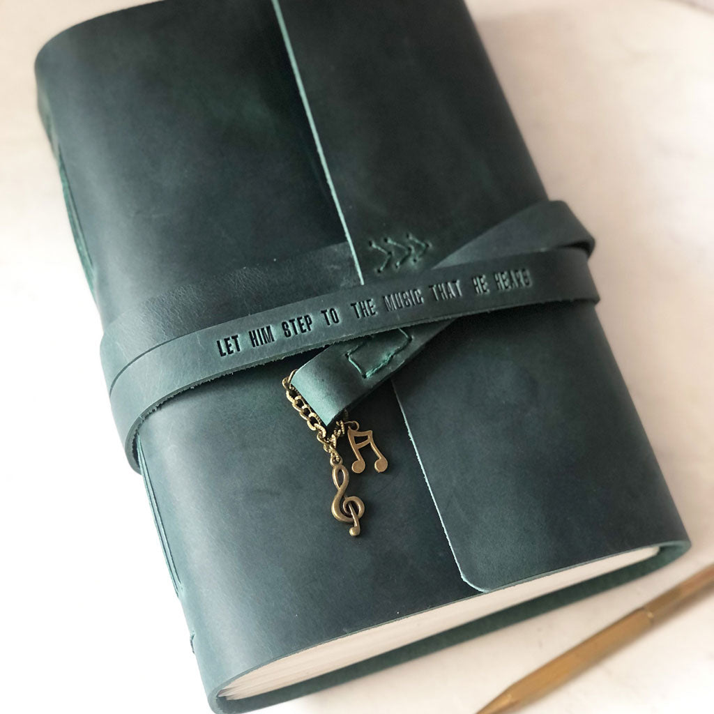 Green leather journal with a decorative musical notes charm on a light background