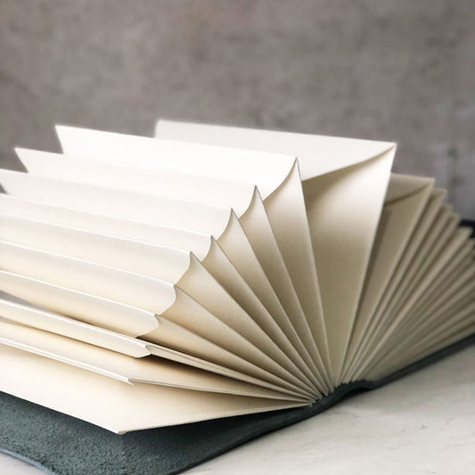 A leather memory book with envelope pages fanned out, showing a clean and minimalist design.
