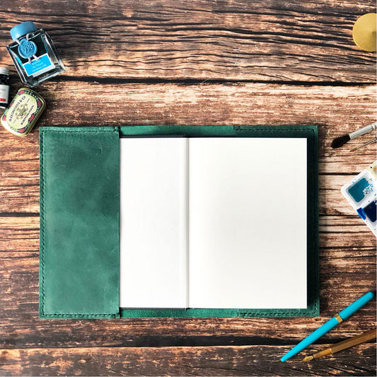 An open green leather sketchbook cover with a hard-backed sketchbook visible inside.