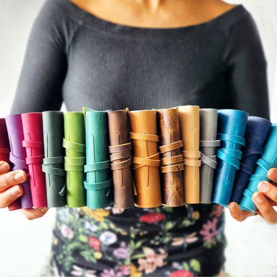 An array of mini leather notebooks in various colors, held between fingers, showcasing the different colors and textures of the leather.