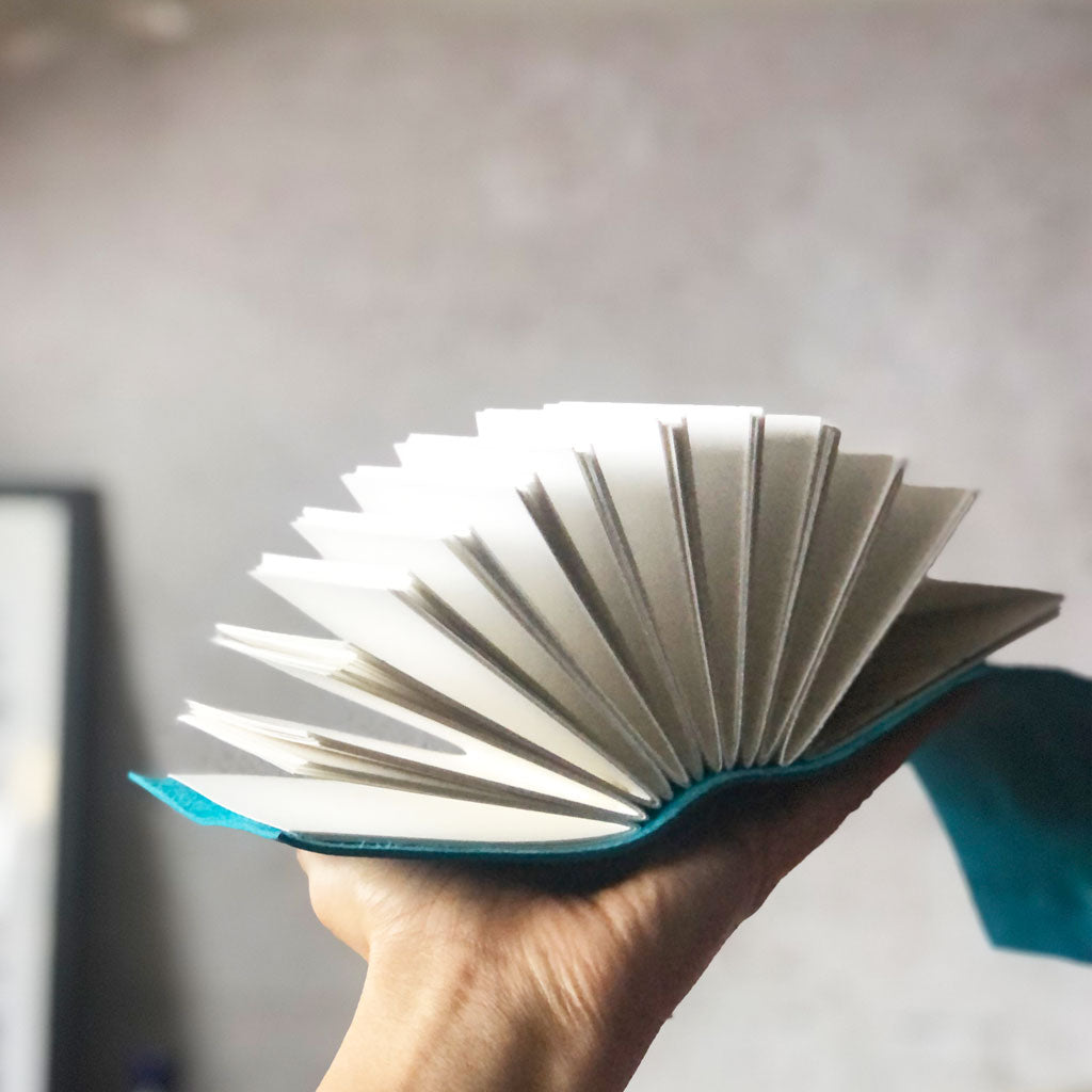 Small A7 leather journal held open in a hand with pages fanned out