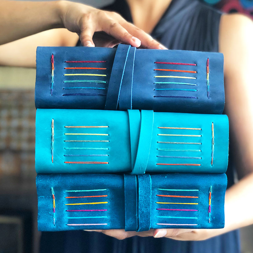 Stack of handmade leather journals with rainbow binding