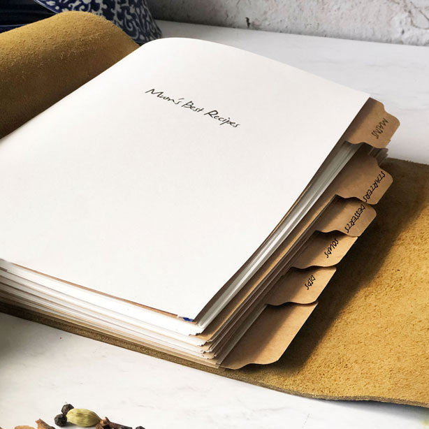 A leather-bound recipe book with tab dividers visible, lying open on a surface.
